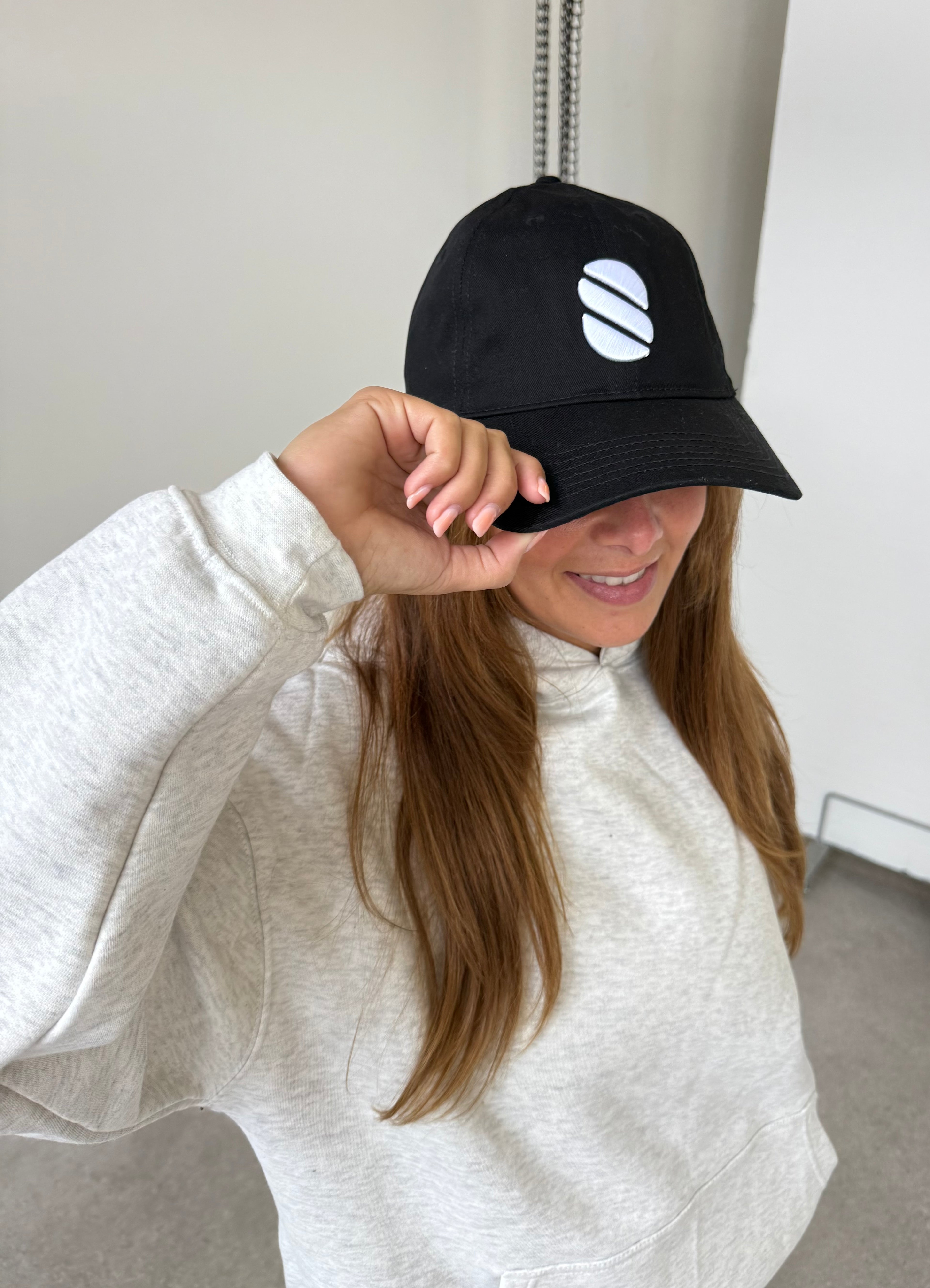 Person wearing a black cap with a white logo, smiling indoors.