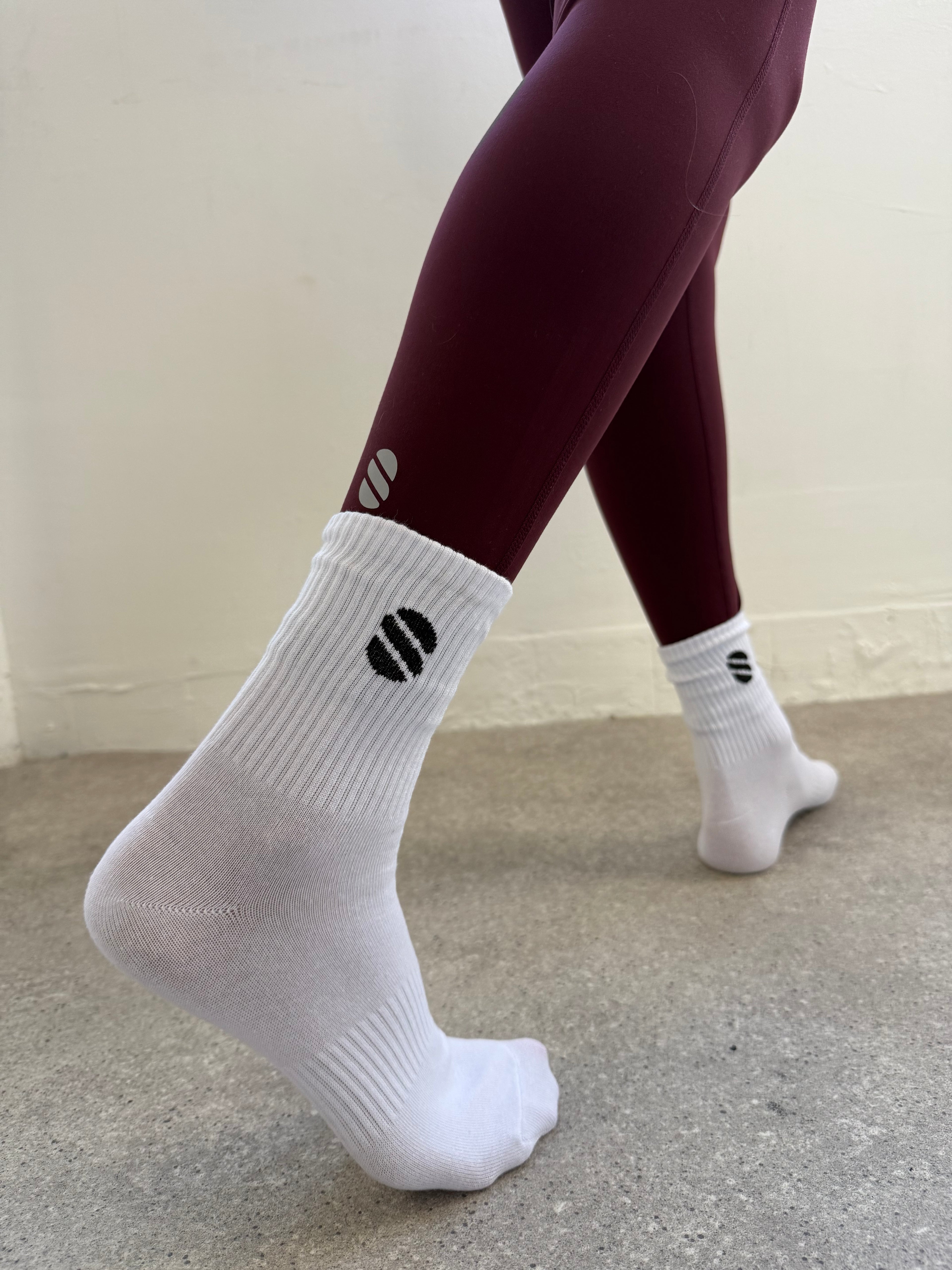 White socks with a navy logo worn by a person against a neutral background