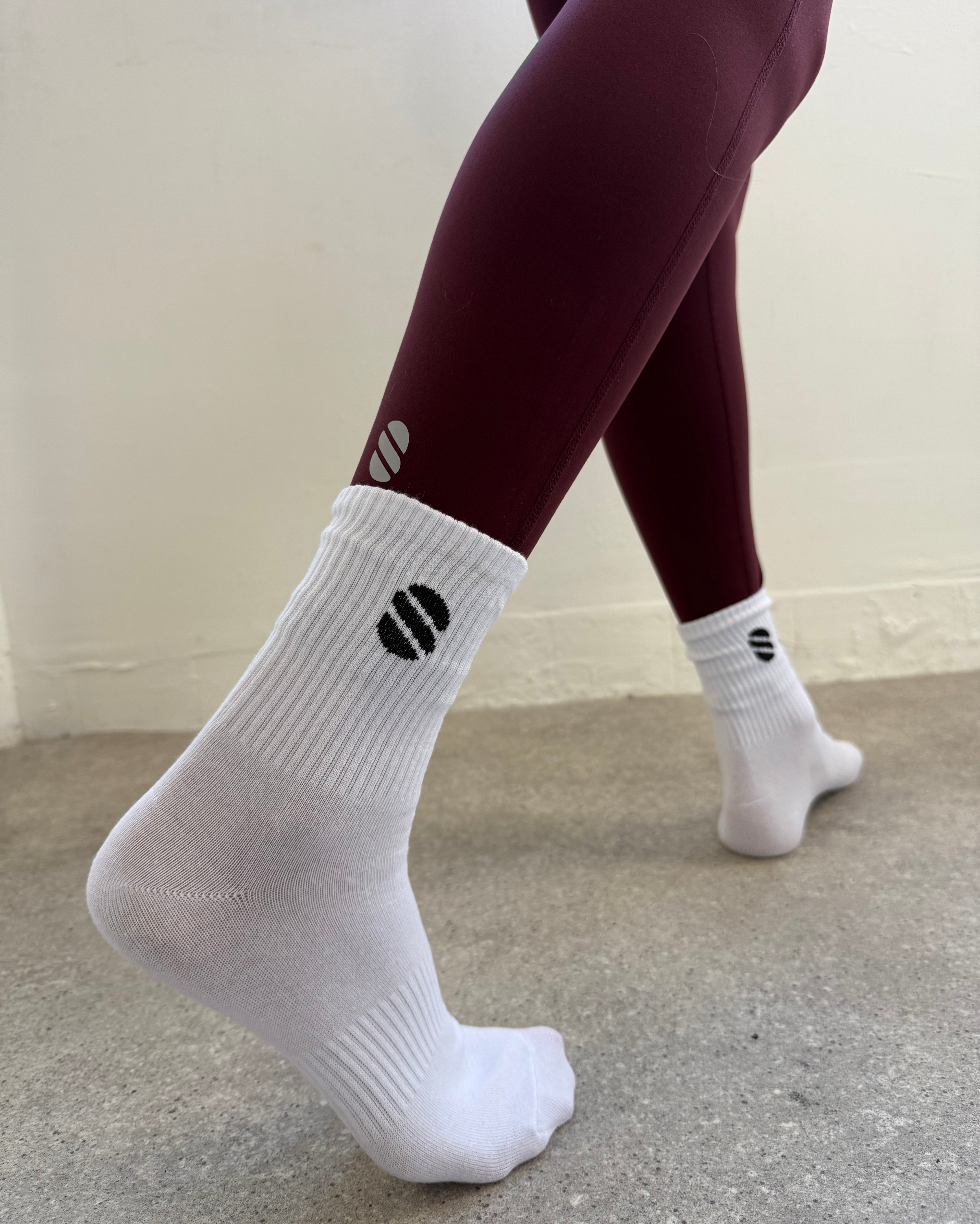 White socks with a navy logo worn by a person against a neutral background