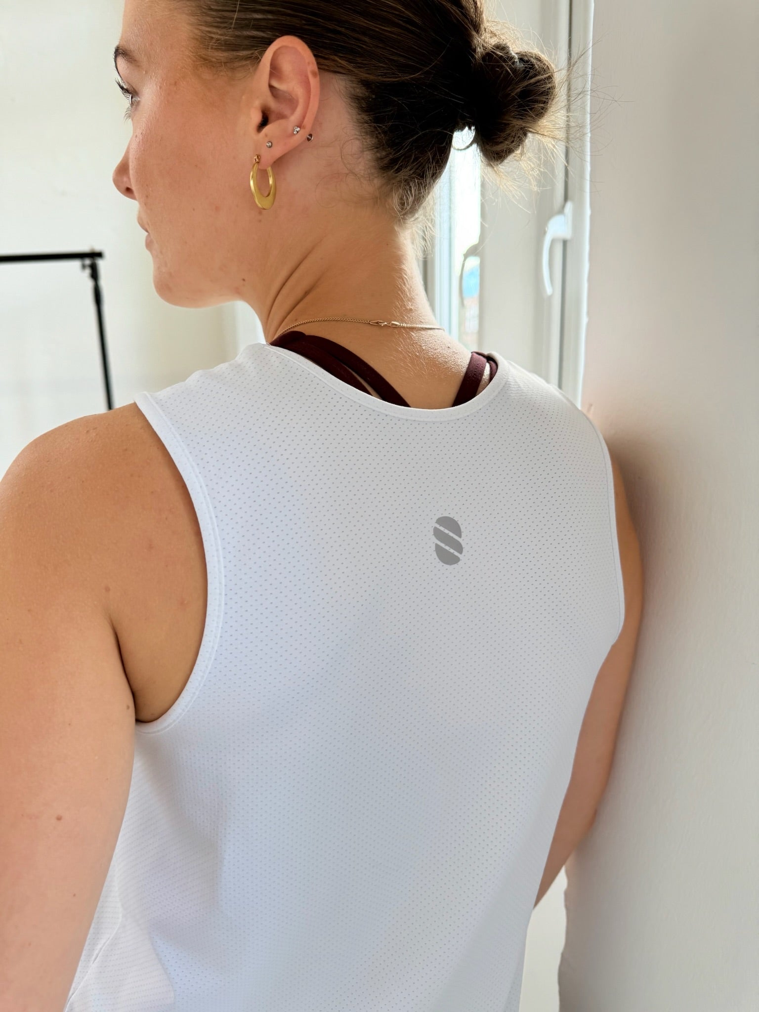 Person wearing a white sleeveless top with a logo, standing indoors.