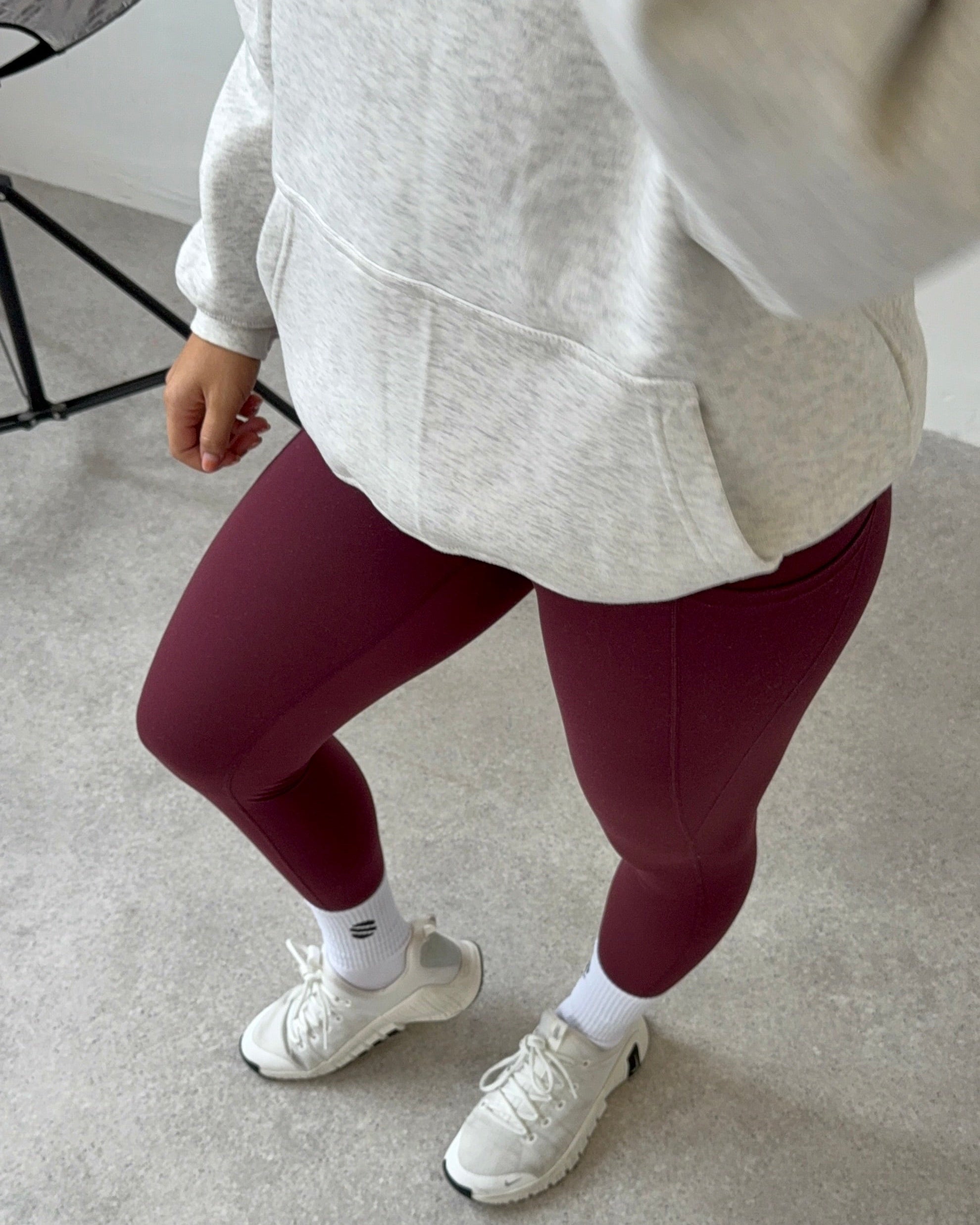 Person wearing maroon leggings, white sneakers, and a light gray hoodie on a neutral background