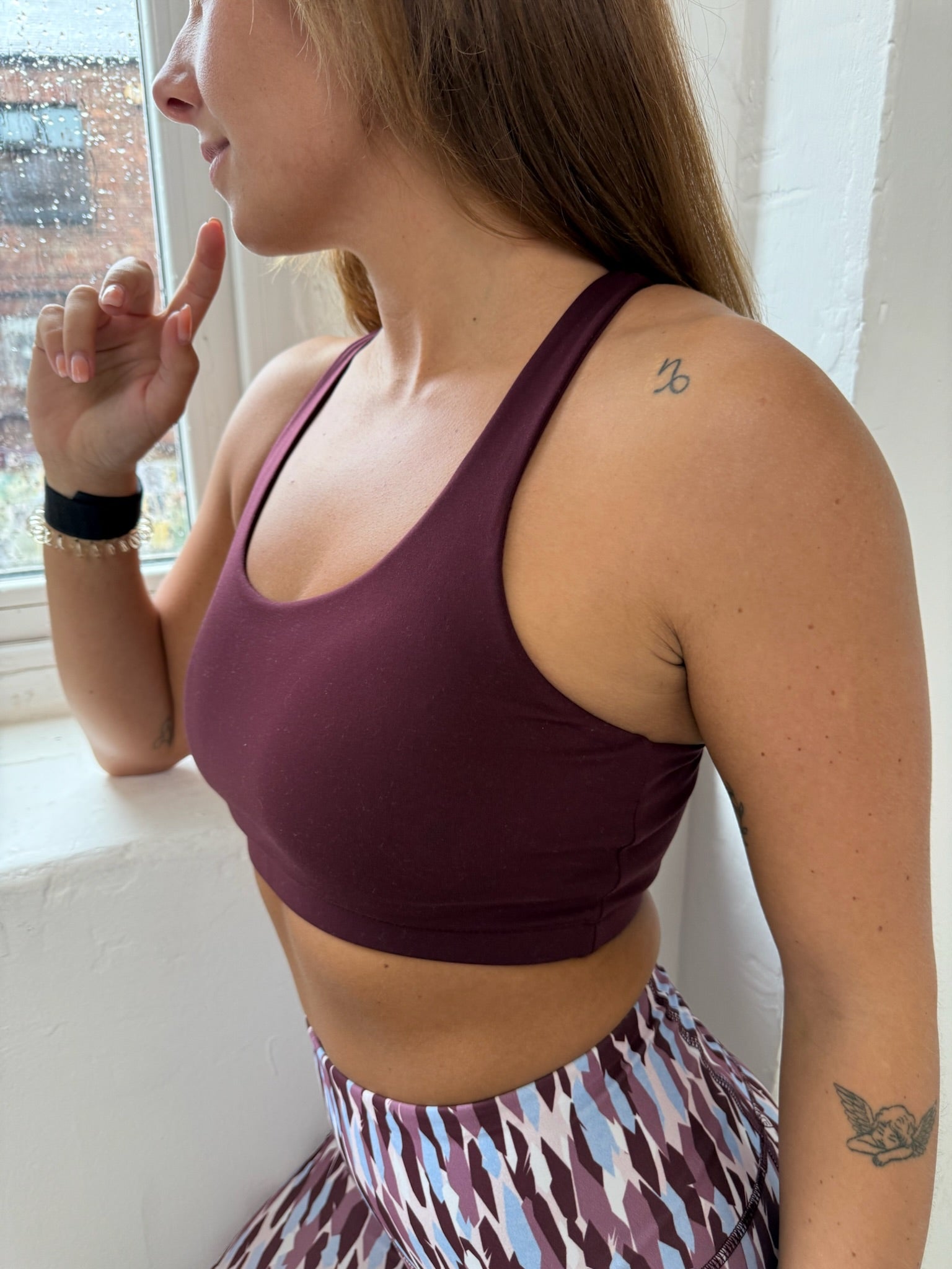 Person wearing a dark cherry sports bra and patterned leggings indoors.