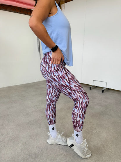 Person wearing a light blue tank top and patterned leggings in an indoor setting.