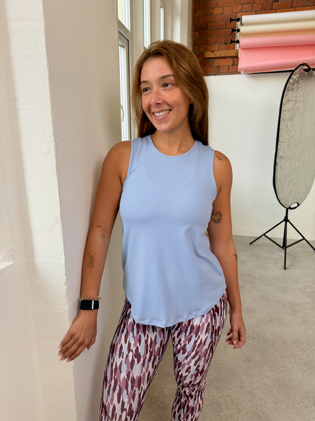 Woman wearing a light blue sleeveless top and patterned leggings indoors.