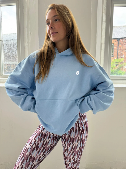 Person wearing a light blue hoodie and patterned pants standing indoors.