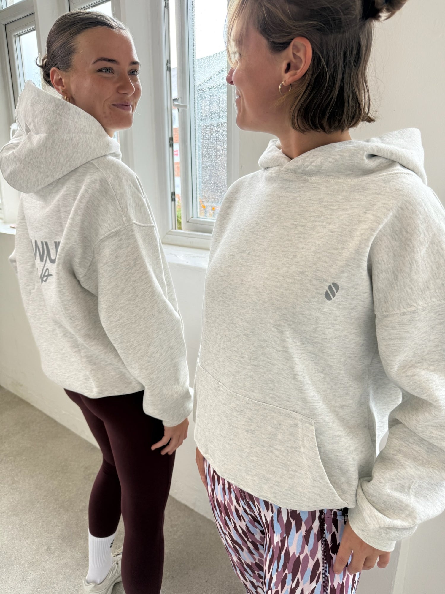 Two people wearing gray hoodies with visible brand logos, standing indoors.