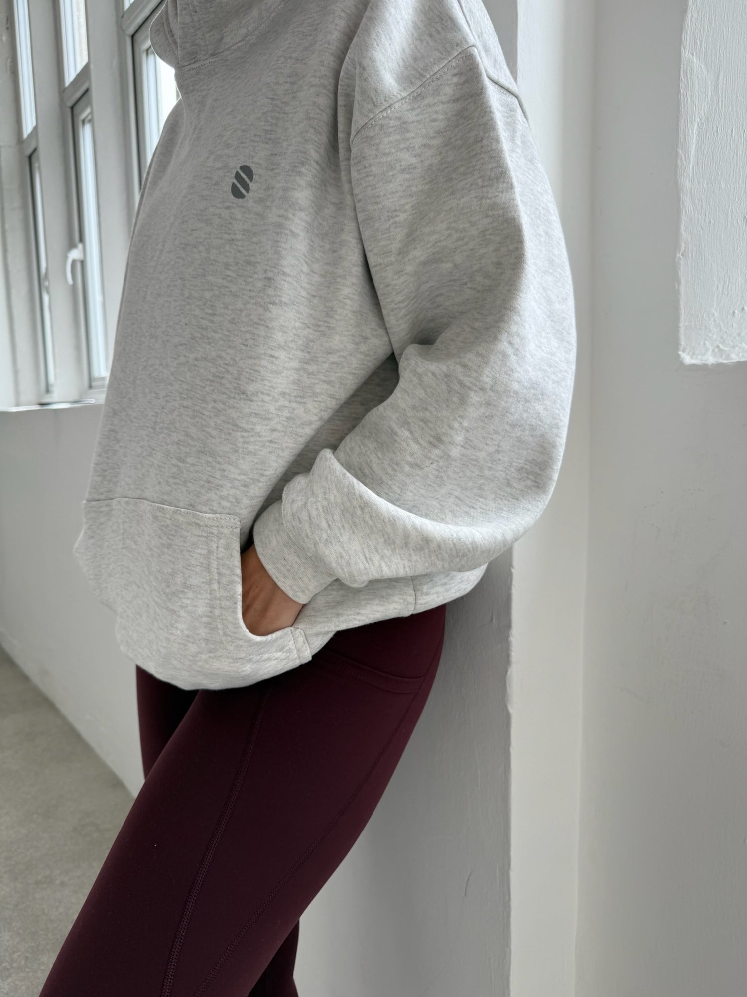 Person wearing a gray sweatshirt and maroon leggings against a white wall.