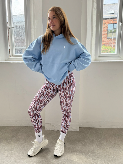 Person wearing a blue sweatshirt and patterned leggings standing in a room with large windows.