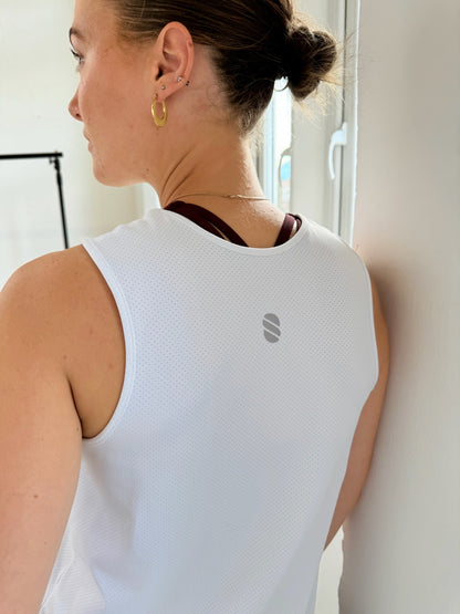Person wearing a white sleeveless top with a logo, standing indoors.