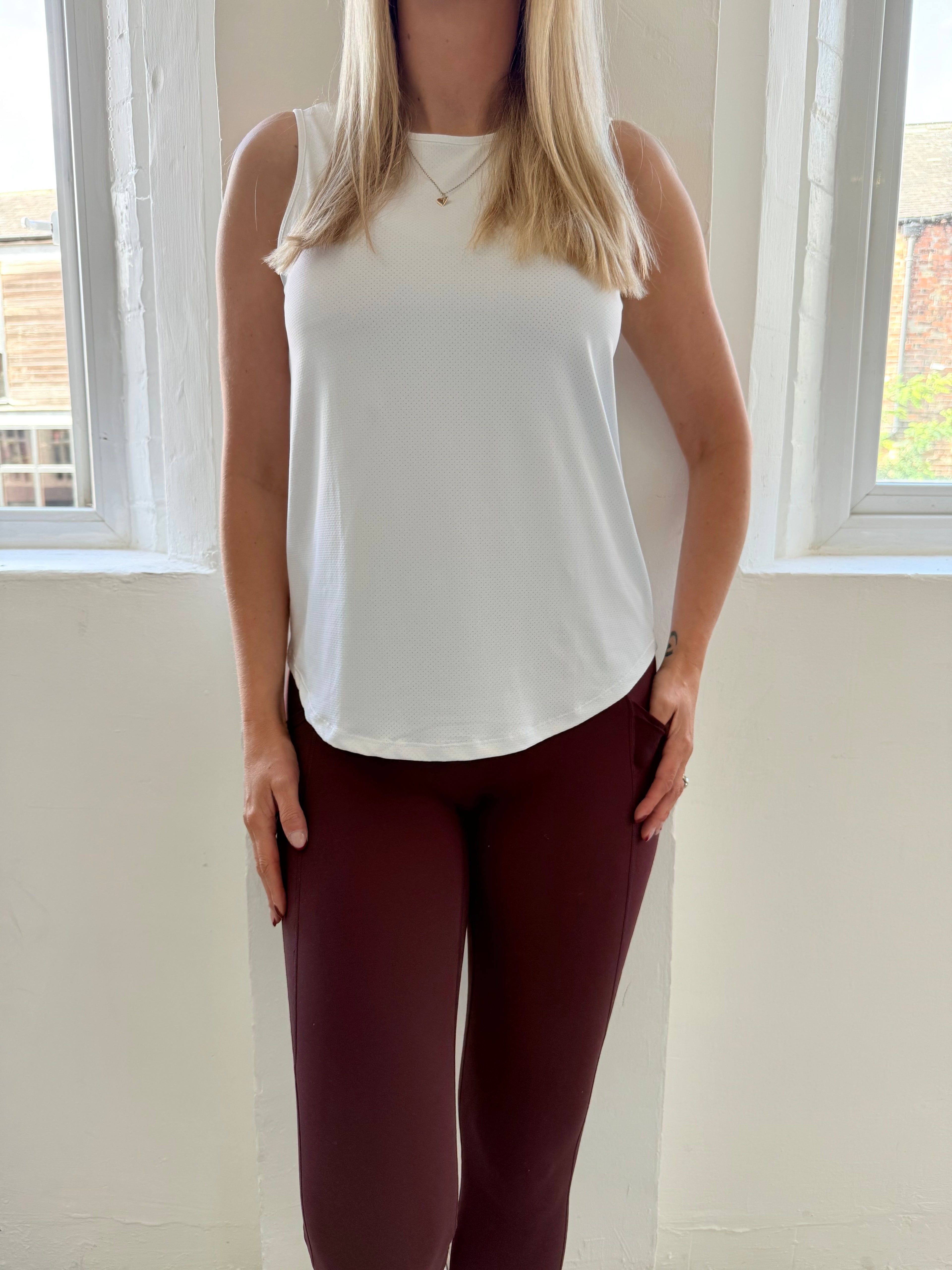 Person wearing a white sleeveless top and maroon leggings indoors.