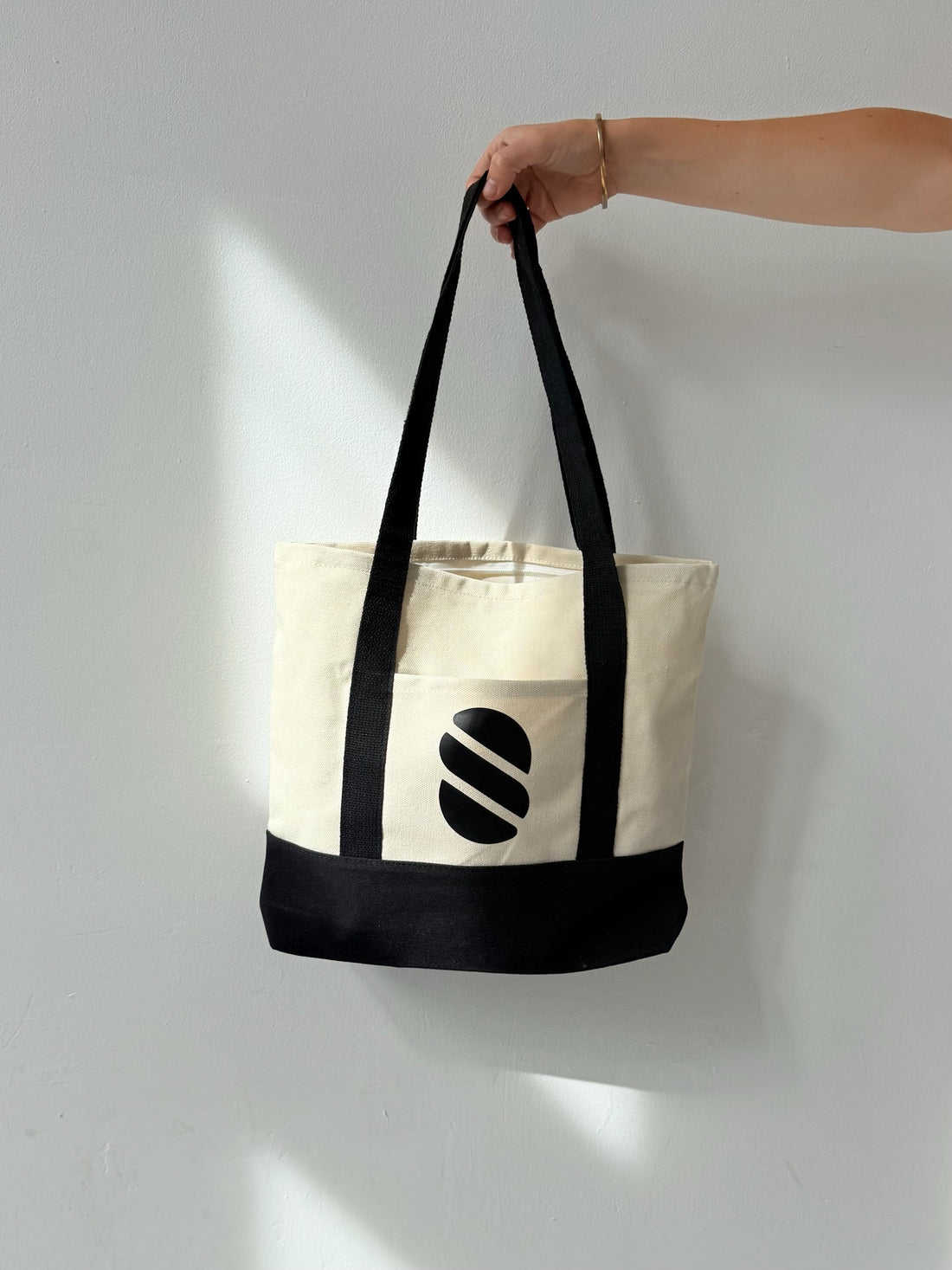 Tote bag with a logo held by a hand against a light gray background