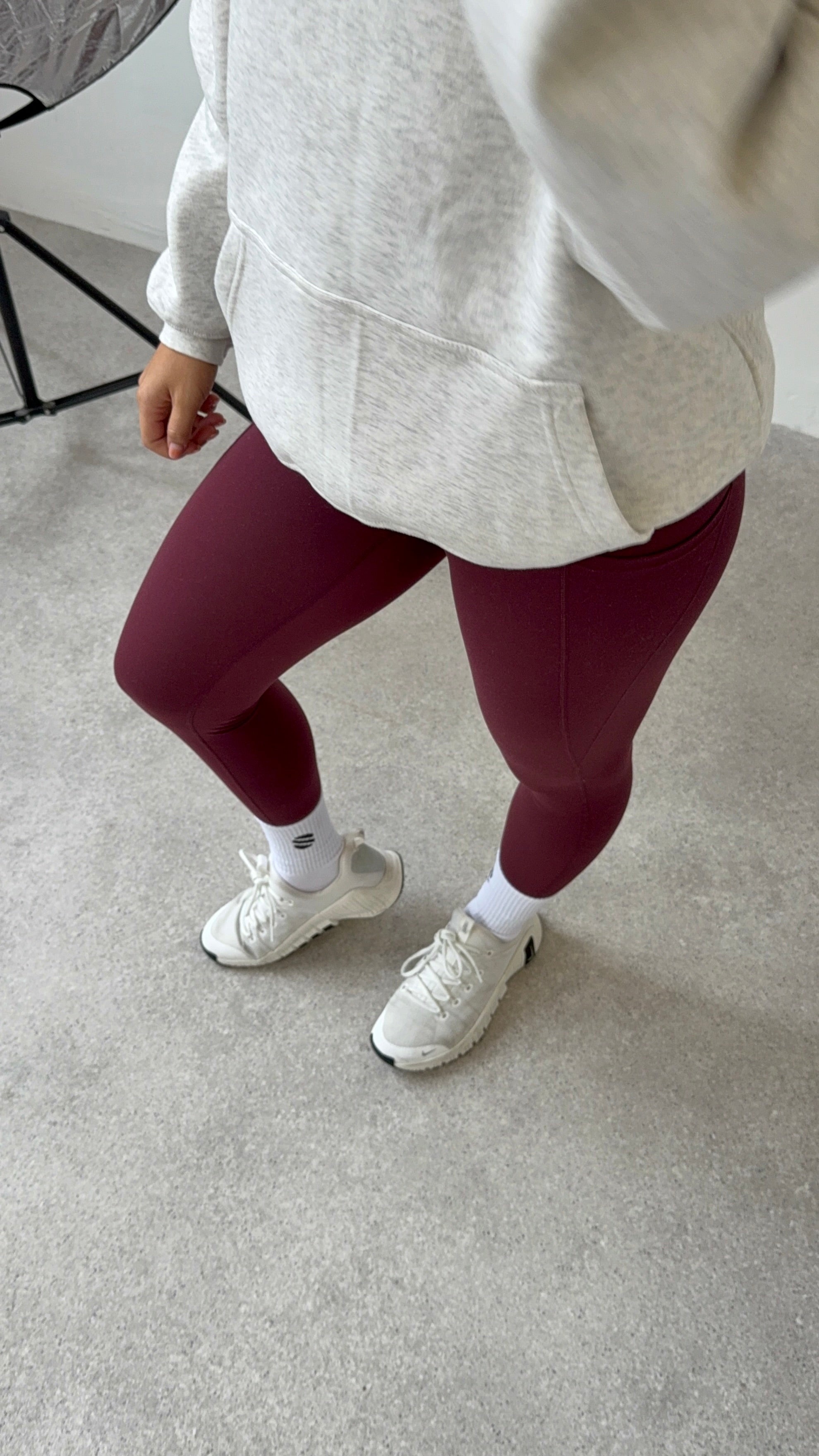 Person wearing maroon leggings, white sneakers, and a light gray hoodie on a neutral background