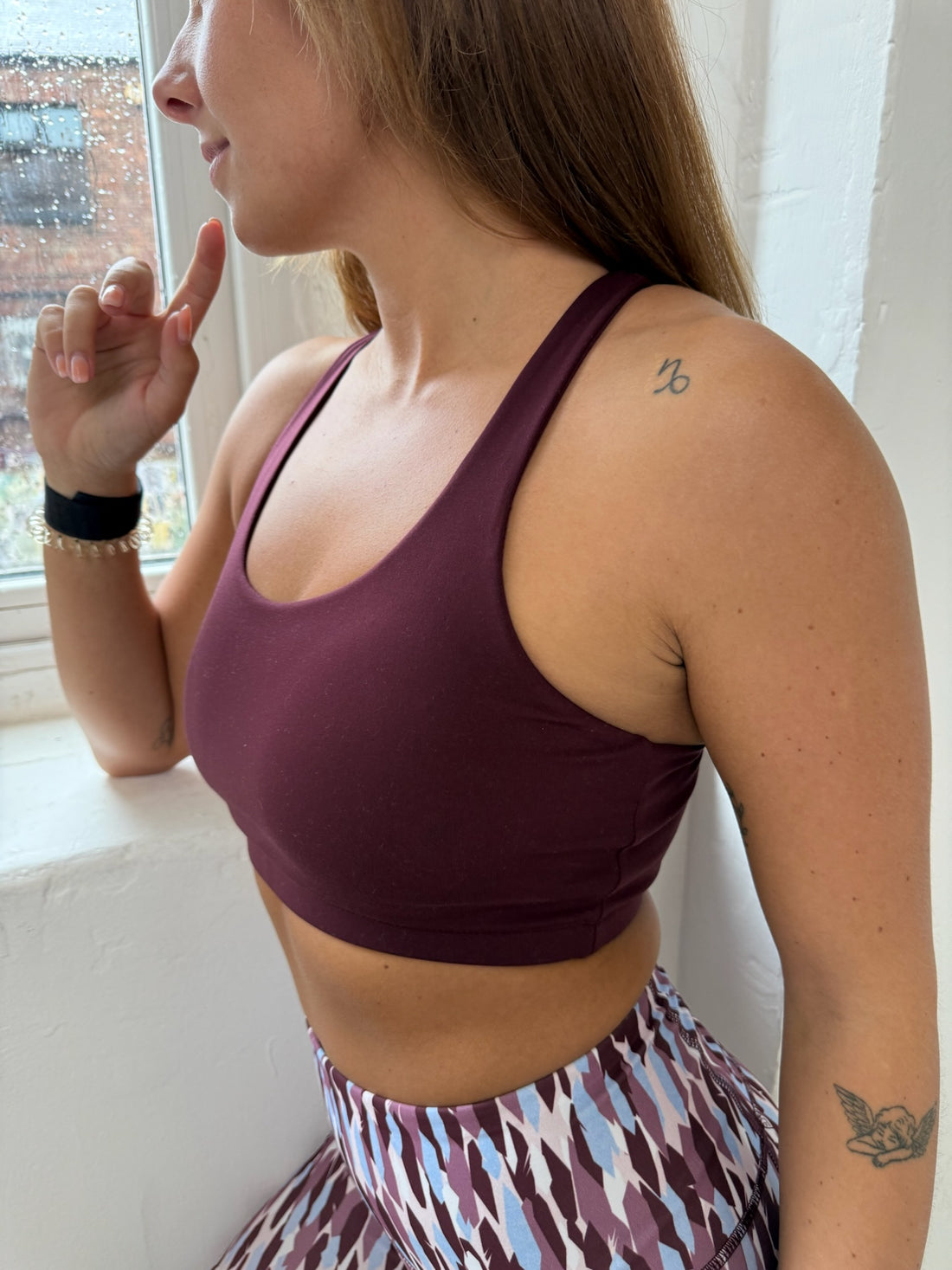 Person wearing a dark cherry sports bra and patterned leggings indoors.